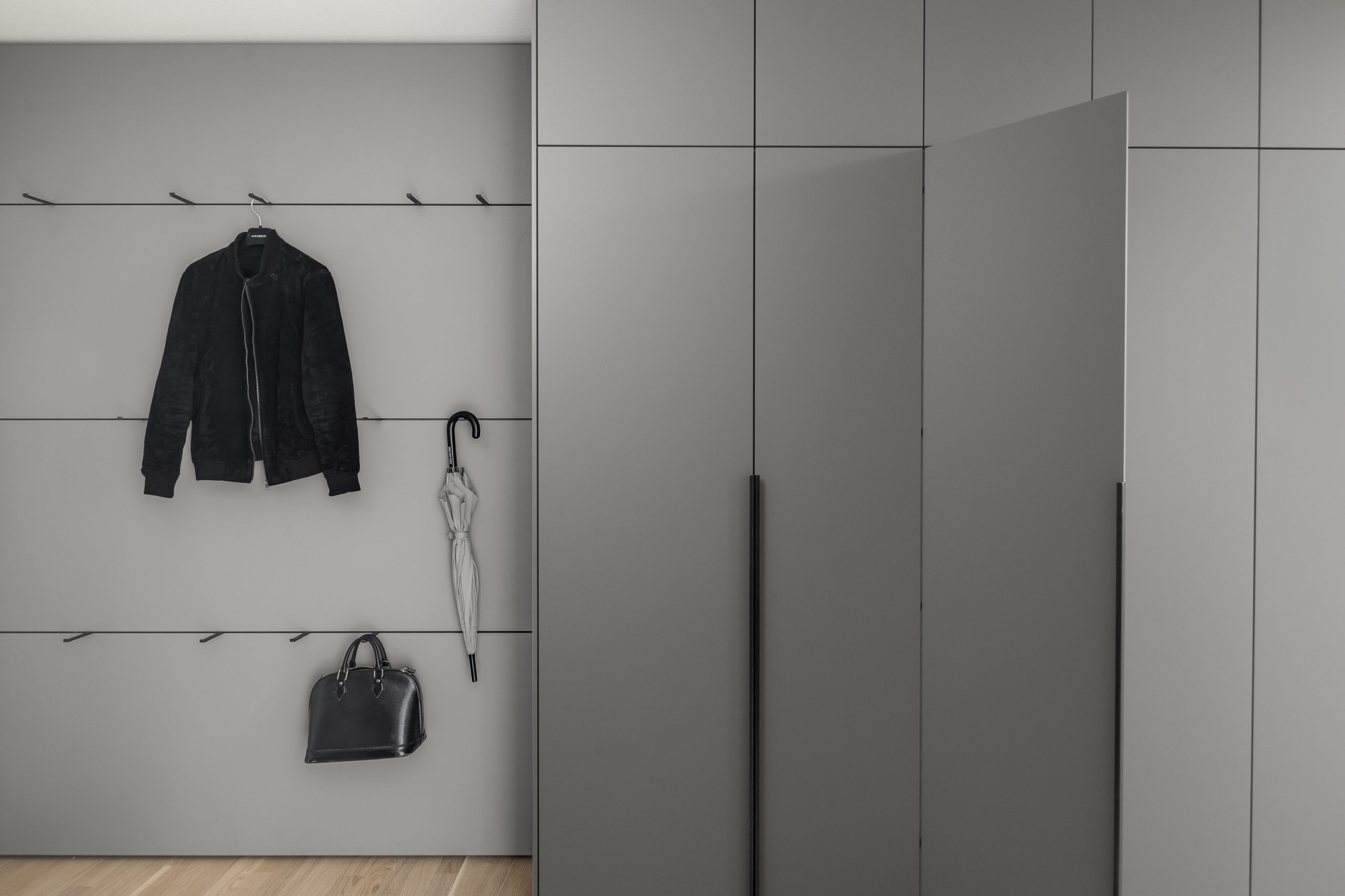 Garderobe mit Wandpaneelen und Kleiderhaken und schwarzen Griffen.