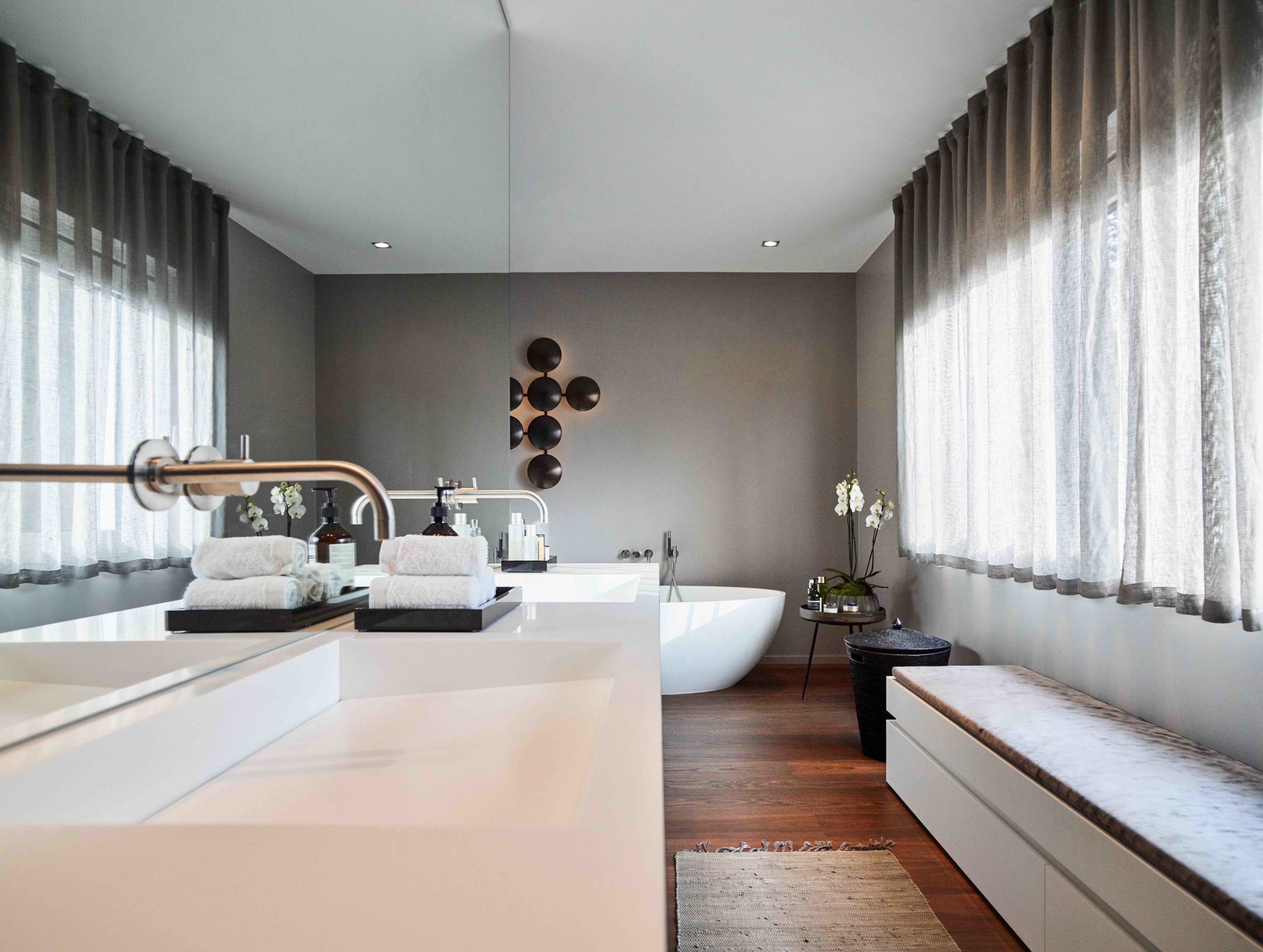 Luxuriöses Badezimmer mit freistehender Badewanne, deckenhohem Spiegel und Tageslicht durch große Fensterfront.