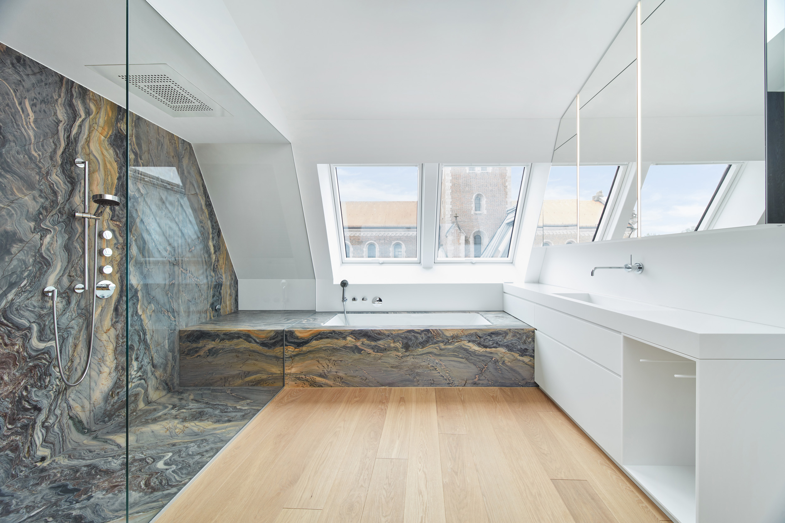 Badezimmer mit Naturstein-Duschbereich, Badewanne und Blick auf eine Kirche