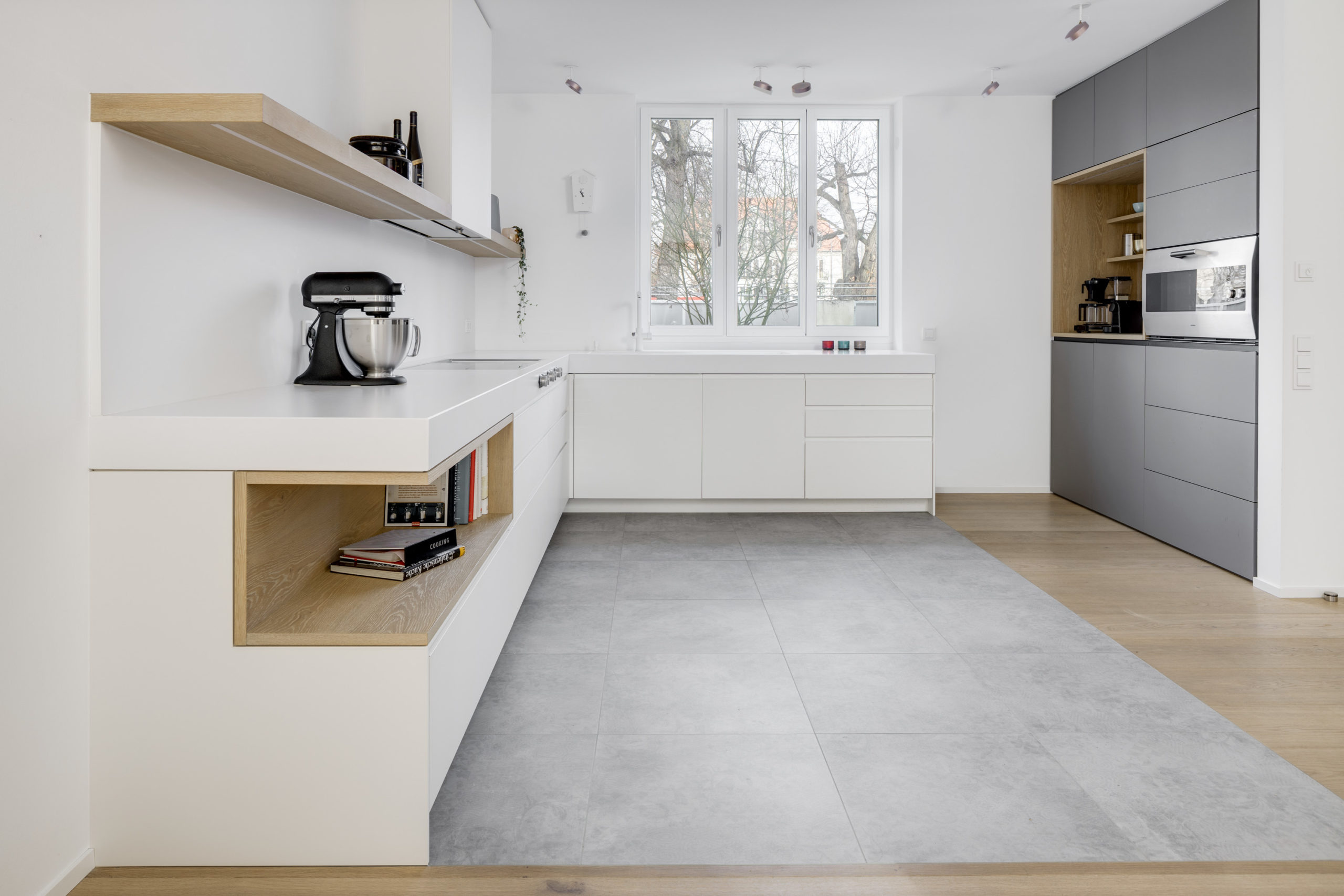 Weiße Designküche mit grauem Hochschrank und Eichenakzenten – klare Linien und integrierte Technik.