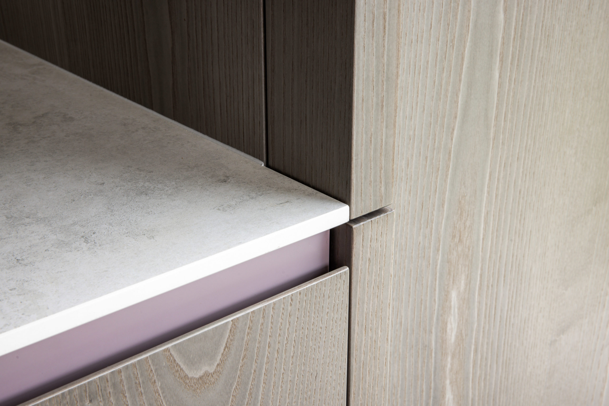 Detailansicht der Küchenfront mit Griffmulde und feiner weißer Arbeitsplatte auf Holzstruktur.