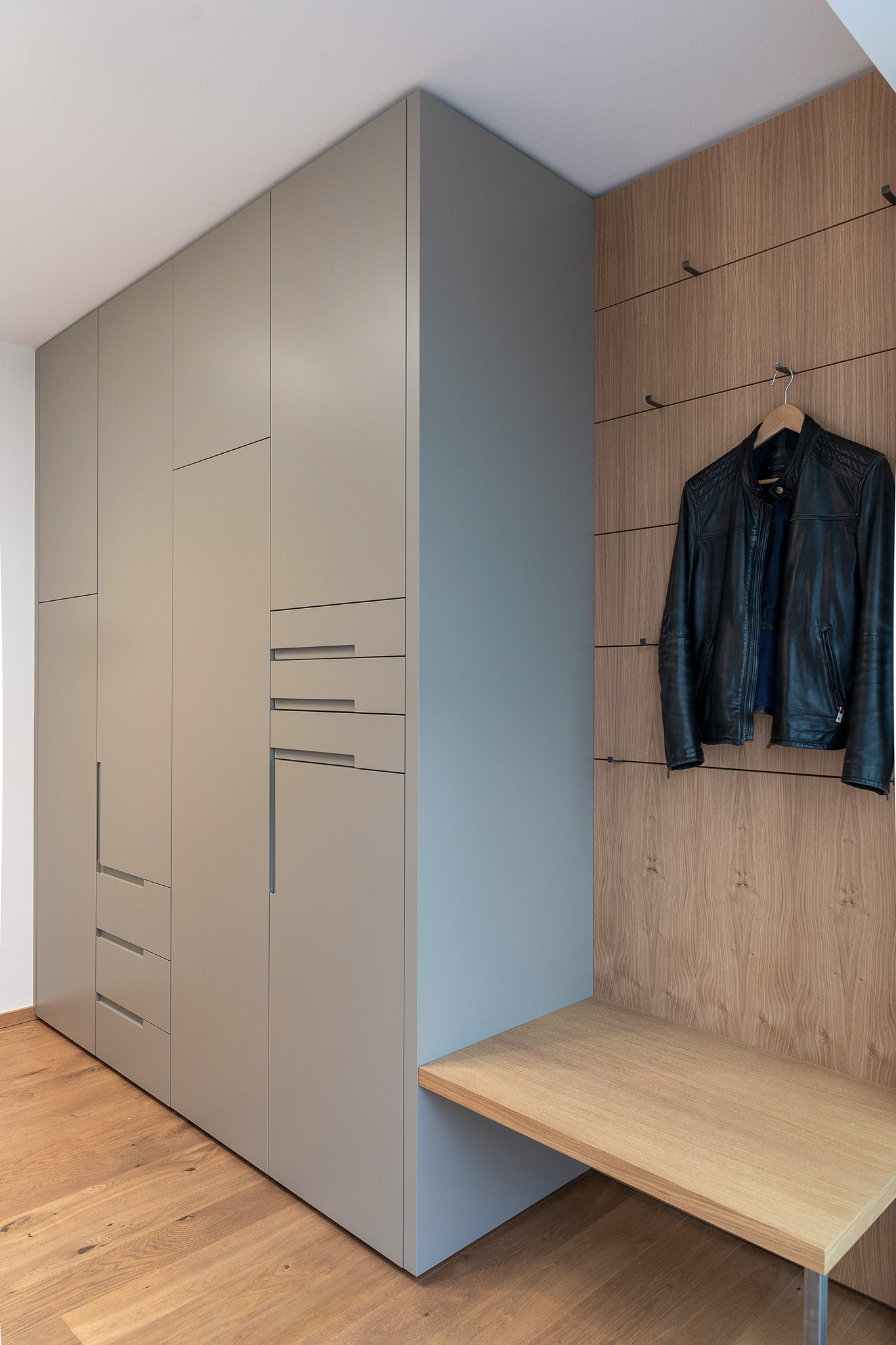 Einbauschrank in Lichtgrau mit integrierten Griffmulden, kombiniert mit Wandverkleidung aus Eiche und Sitzbank im modernen Eingangsbereich.