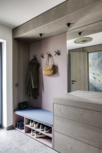Maßgefertigte Garderobe mit gepolsterter Sitzbank, Schuhregal und rosa Rückwand im Eingangsbereich.