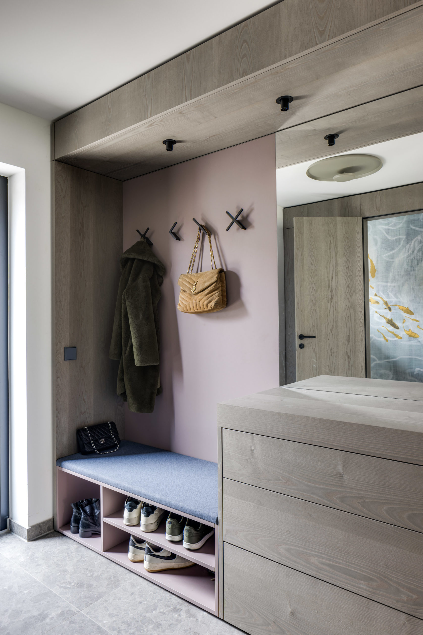 Maßgefertigte Garderobe mit gepolsterter Sitzbank, Schuhregal und rosa Rückwand im Eingangsbereich.