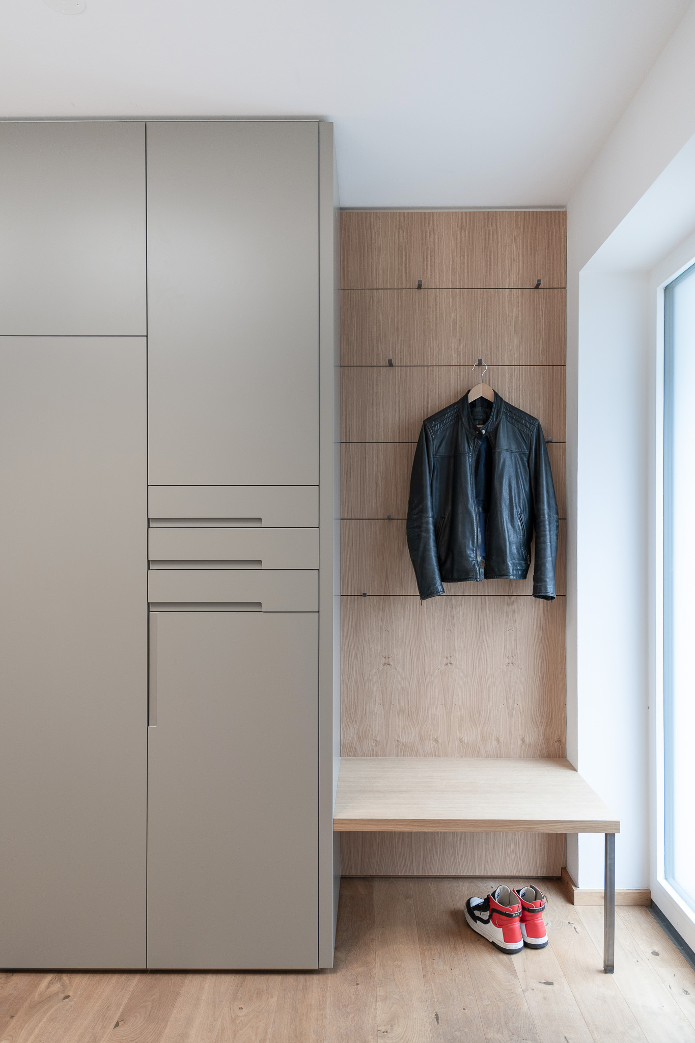 Modernes Garderobenelement mit Sitzbank und Kleiderhaken auf Eiche-Rückwand, minimalistisch gestaltet für den Eingangsbereich.