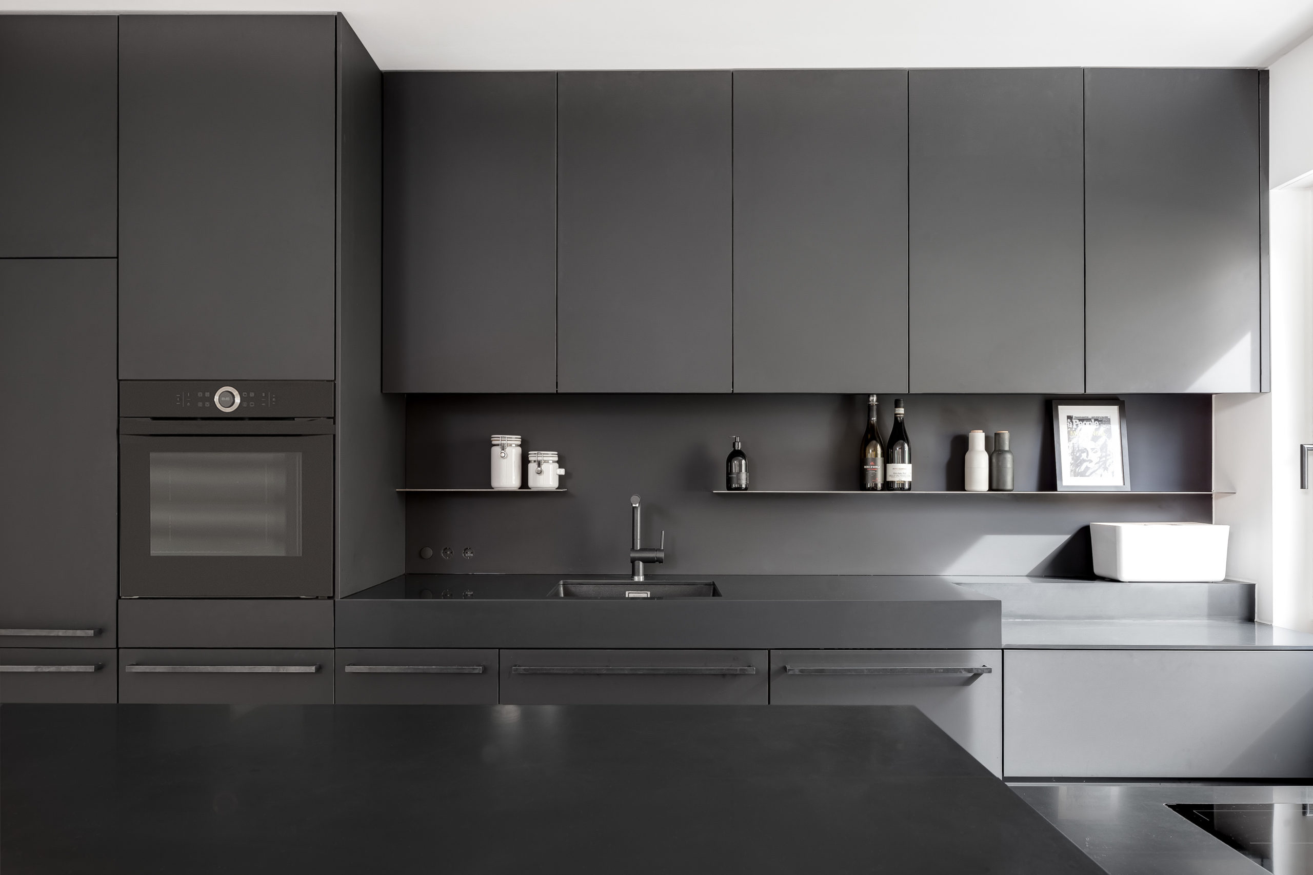 Moderne schwarze Küche mit Induktionskochfeld, grifflosen Fronten und durchgehender Arbeitsplatte aus schwarzem Stahl