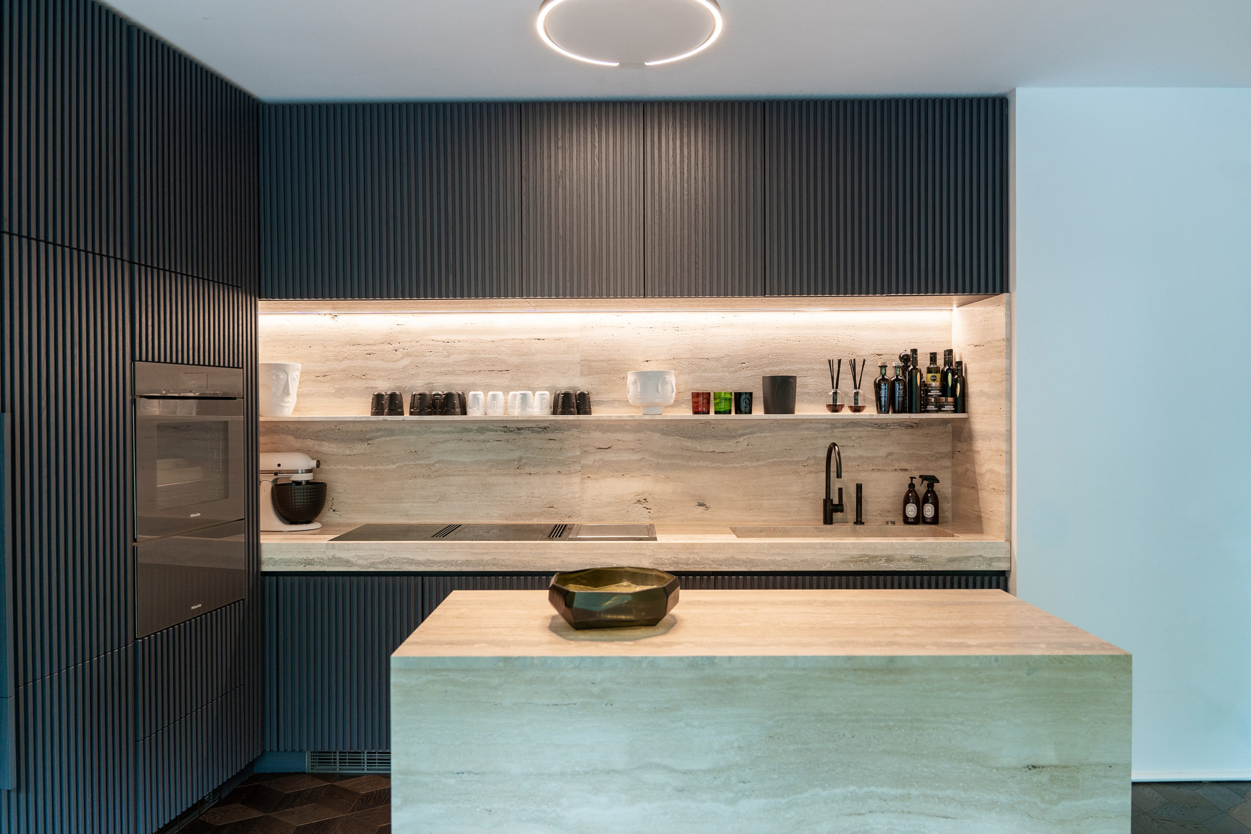 Großzügige Küche mit Travertin-Kücheninsel, vertikaler Lamellenfront, offener Regalfläche und LED-Beleuchtung, modernes Interieur.
