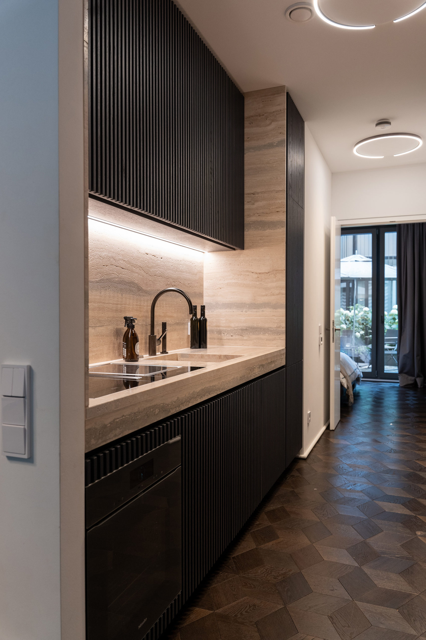 Baristaecke im Küchengang mit Travertinfront, Einbaugeräten und durchdachtem Stauraum, edles Küchendesign.