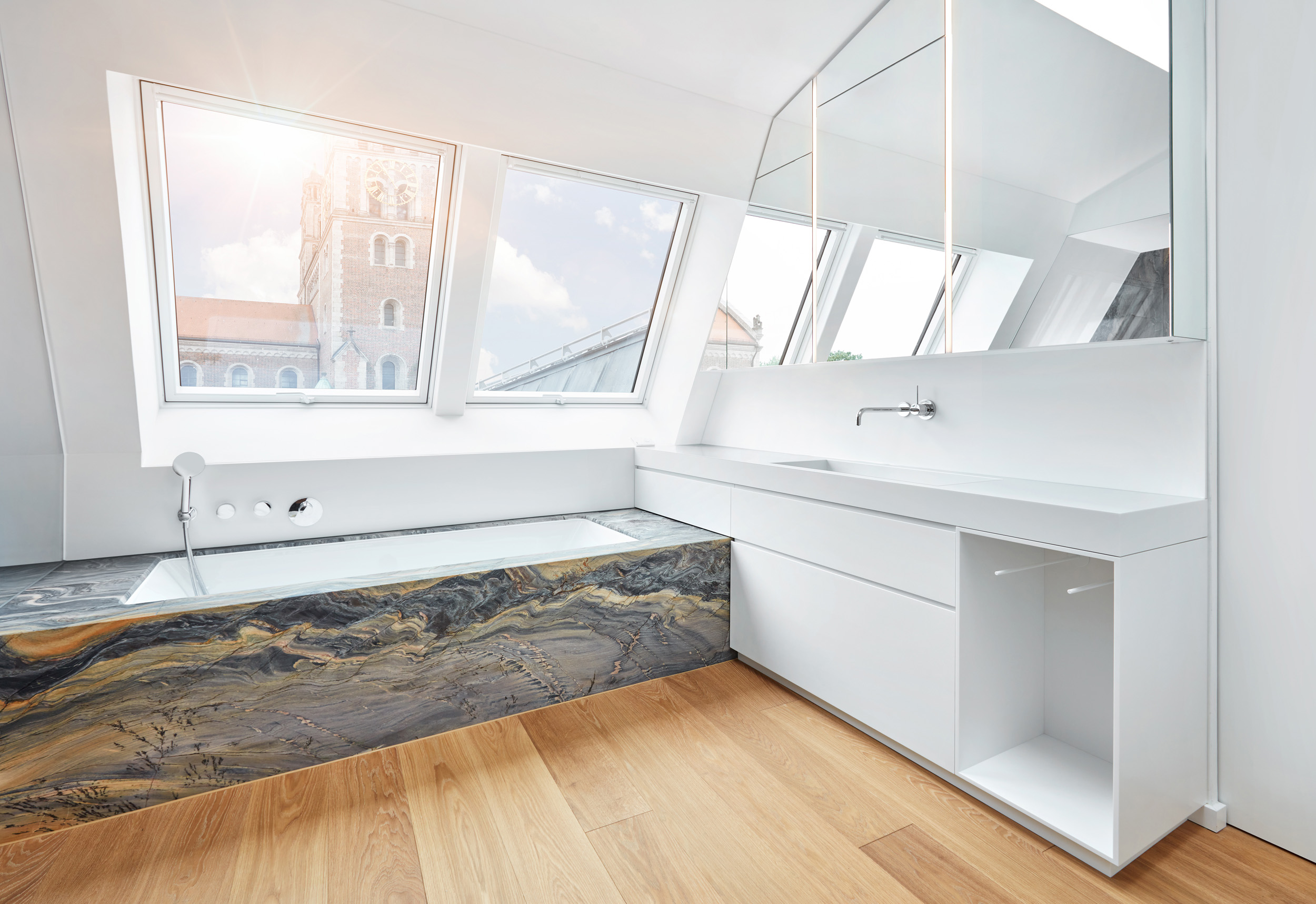 Modernes Badezimmer mit Naturstein-Badewanne unter Dachschräge und Ausblick auf Kirche