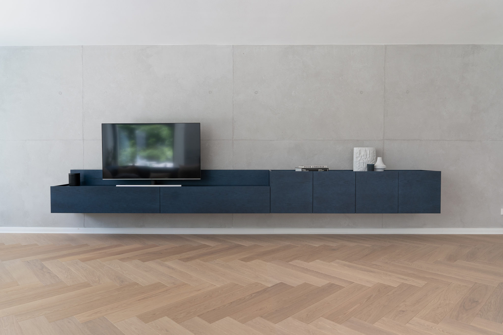 Modernes Wand-Sideboard in blauschimmerndem Tabu-Furnier vor Sichtbetonwand – minimalistisches Möbelkonzept mit schwebender Optik.