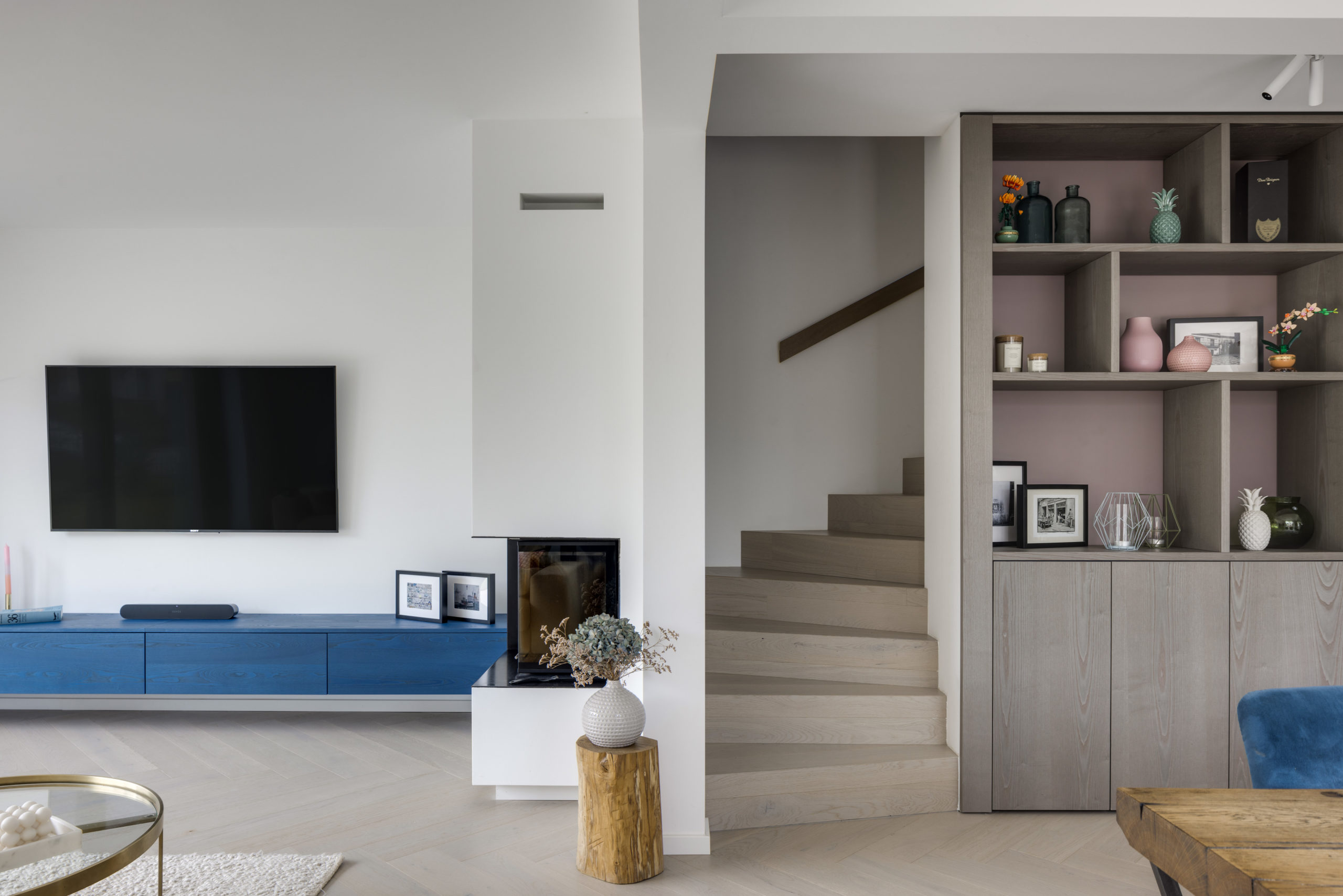 Übergang vom Wohnbereich zur Treppe mit maßgefertigtem Regal in grauem Holz mit rosa Akzentwand.