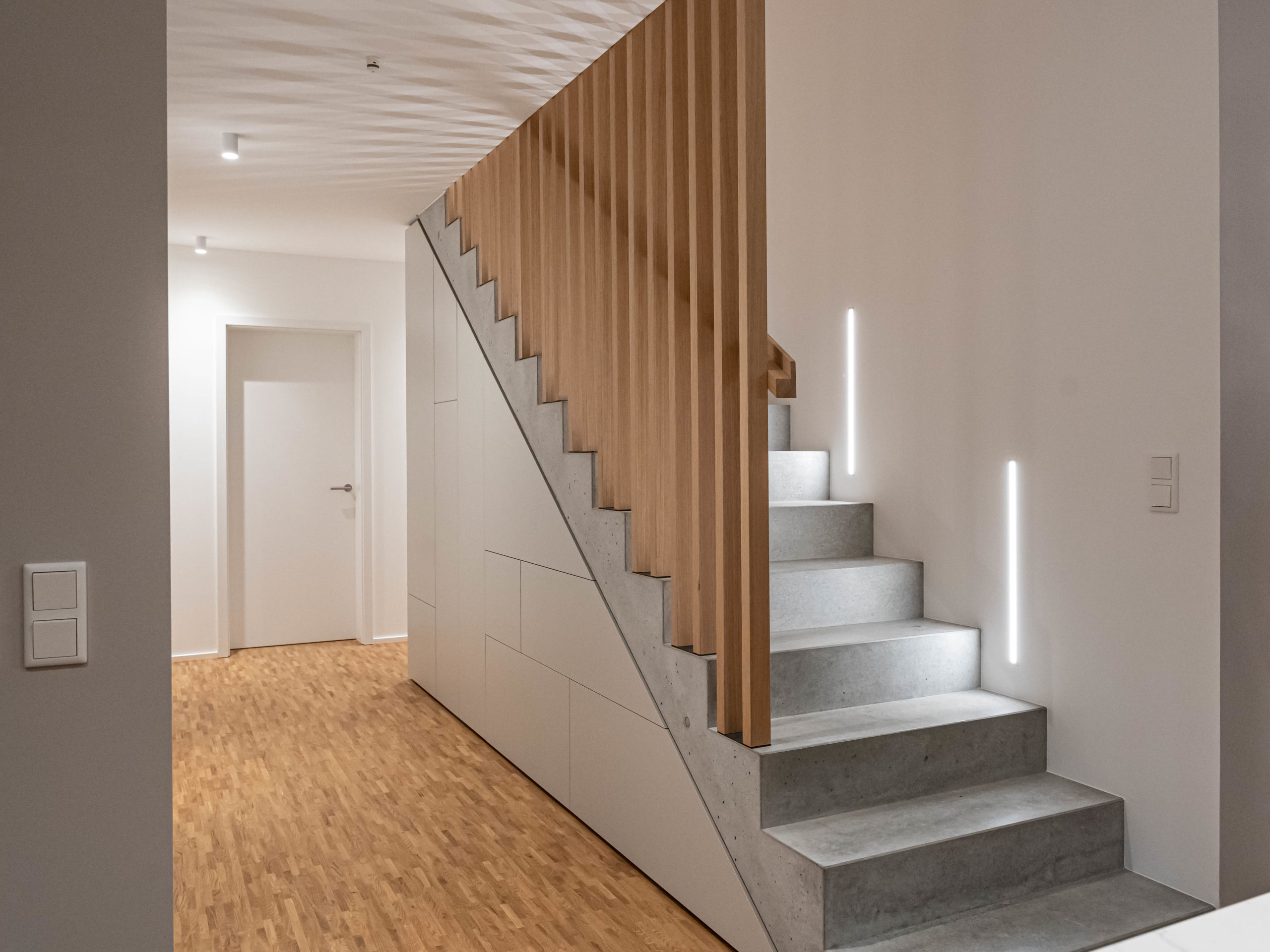Maßgefertigter Einbauschrank unter Betontreppe mit durchgehendem Fugenbild im modernen Flur