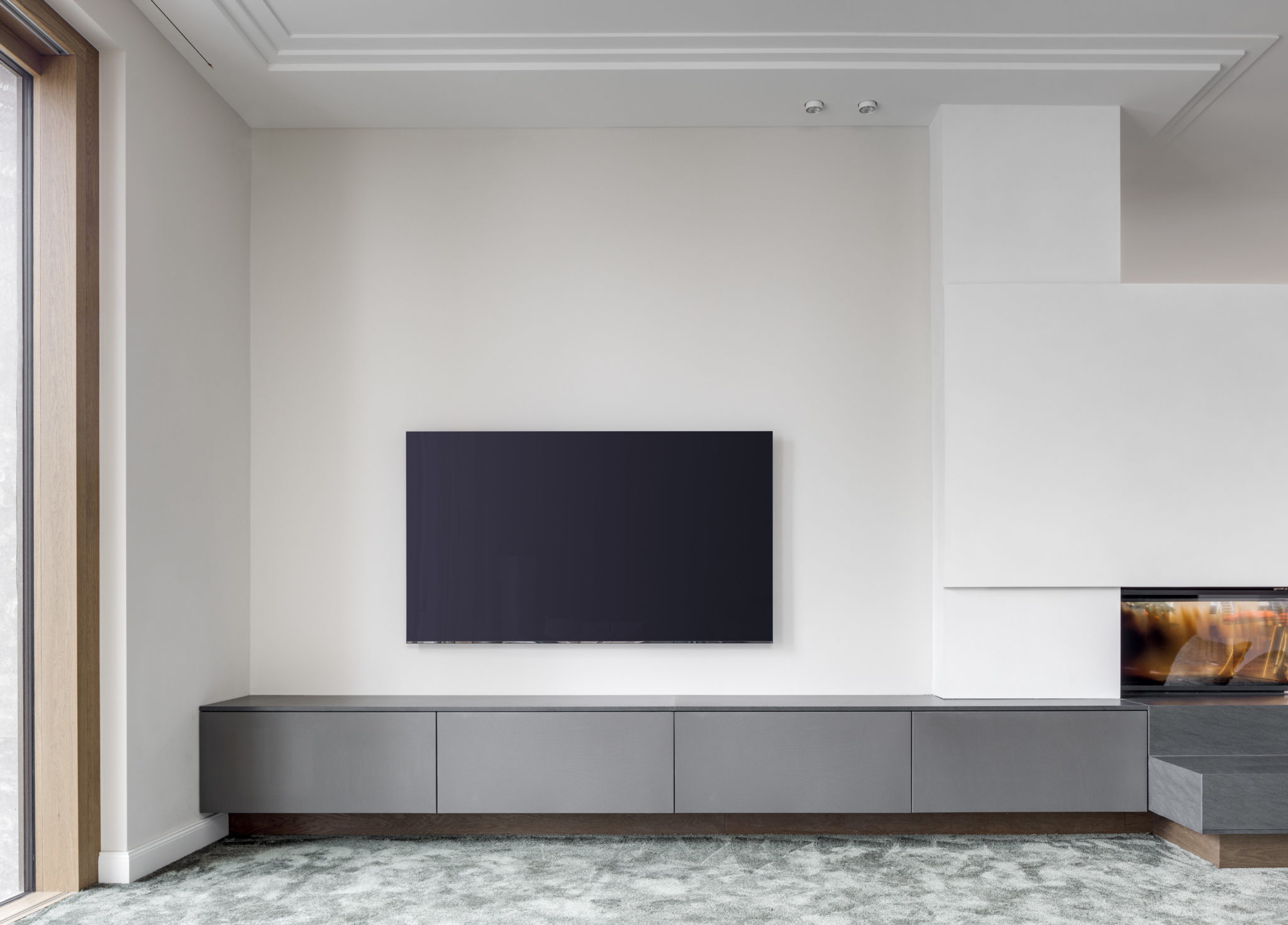 Wandhängendes Lowboard in grauer Oberfläche mit modernem Fernseher und Kaminbereich