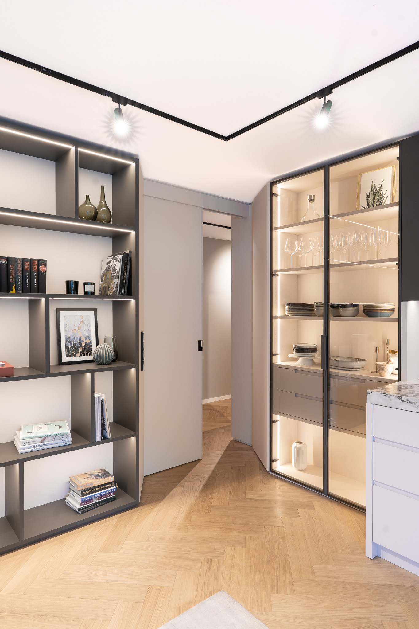 Offene Wohnwand mit angrenzender moderner Küche und beleuchteter Glasvitrine, Innenarchitektur München