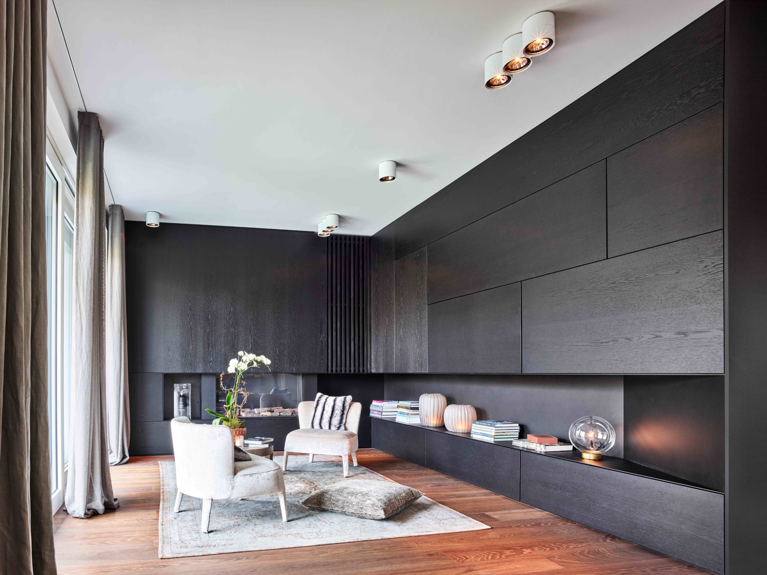 Modernes Wohnzimmer mit maßgefertigten, schwarzen Einbaumöbeln aus Eiche, dekorativem Licht und stilvollem Sitzbereich.