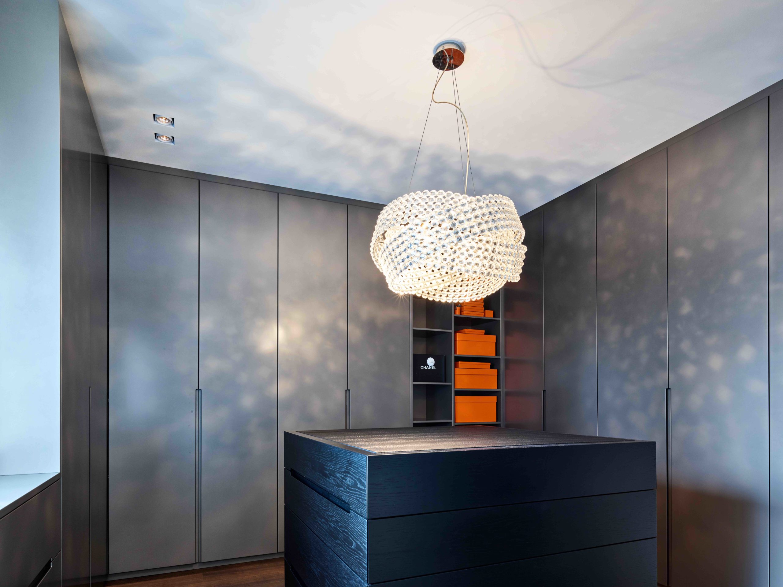 Moderne graue Ankleide mit umlaufenden Schränken, Mittelblock und beleuchteten Regalen mit Hermes-Boxen